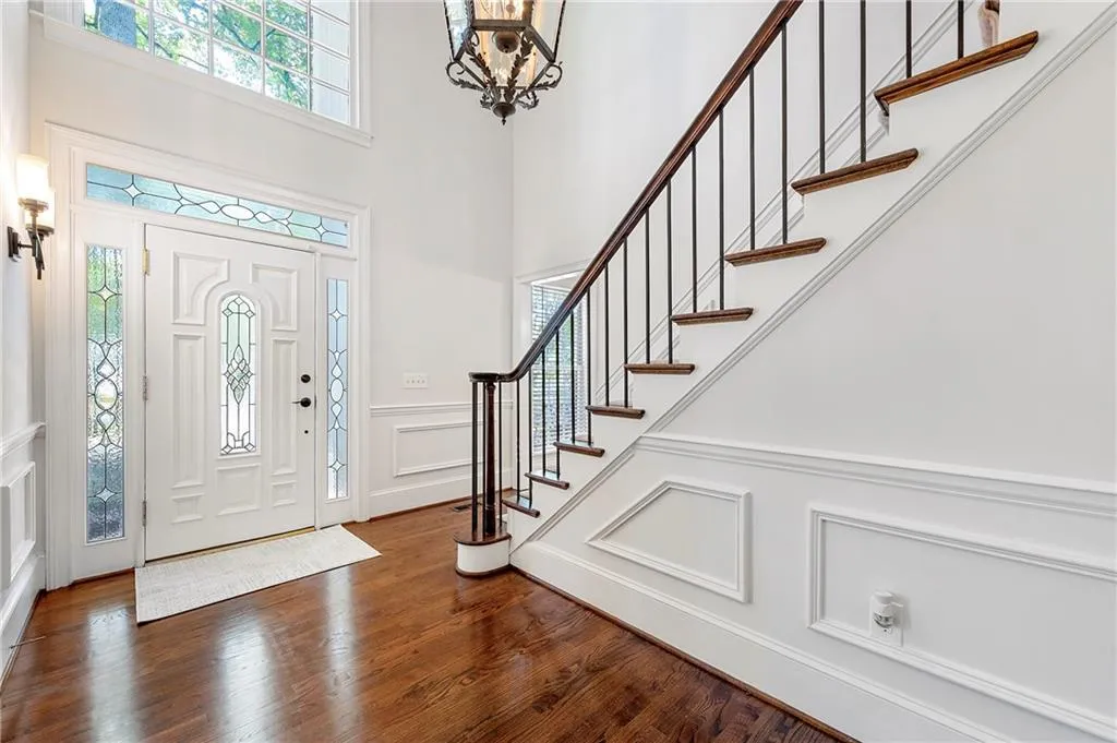 Foyer entrance with a decorative wall, stairs, dark wood-style flooring, a chandelier, and wainscoting