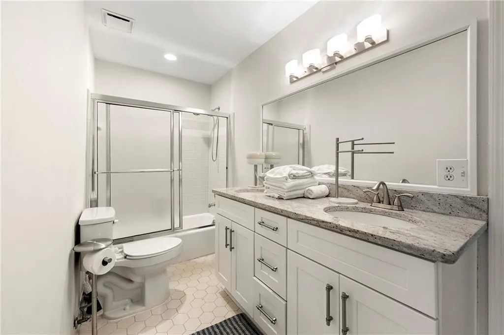 Bathroom featuring double vanity, tile patterned floors, toilet, shower / bath combination with glass door, and recessed lighting