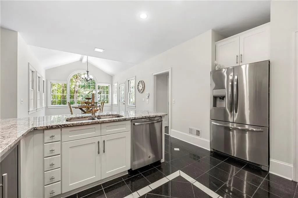 Kitchen featuring appliances with stainless steel finishes, granite floors, baseboards, white cabinetry, and light stone counters
