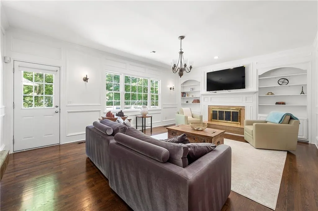 Living area featuring built in features, a glass covered fireplace, a decorative wall, ornamental molding, and dark wood-style flooring