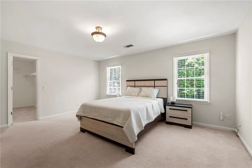 Bedroom featuring multiple windows, light carpet, baseboards, and a walk in closet