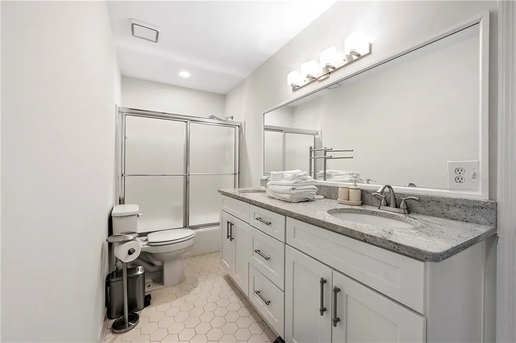Full bath with double vanity, toilet, tile patterned flooring, shower / bath combination with glass door, and recessed lighting