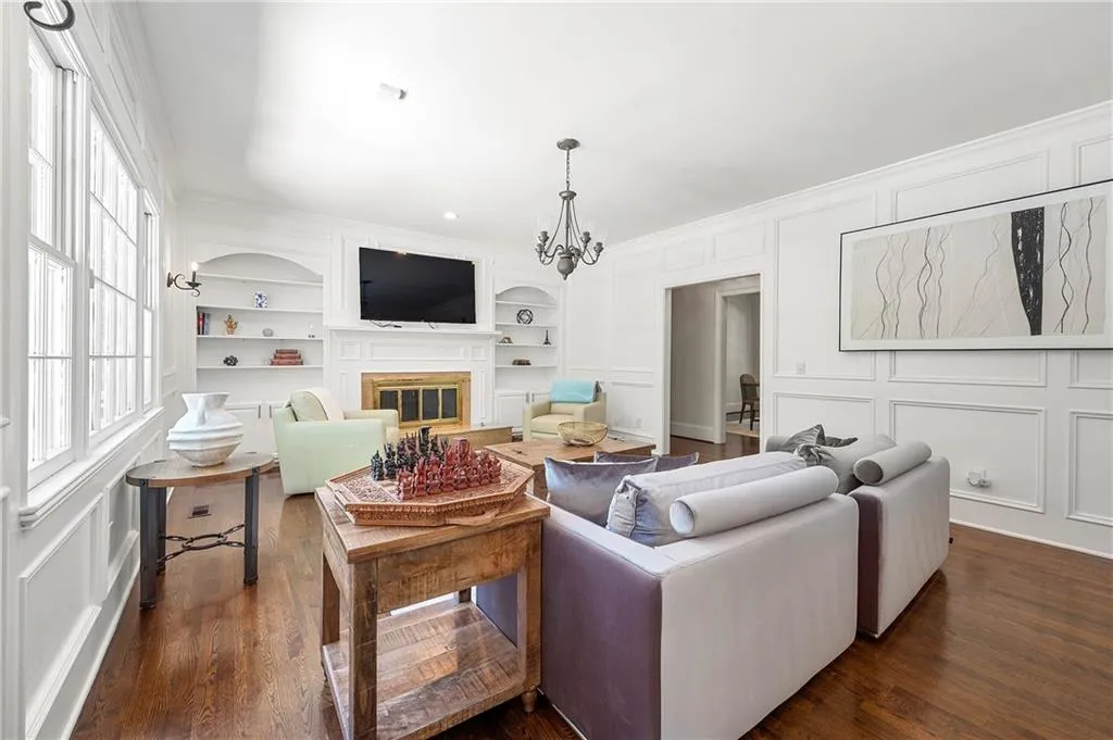 Living room with a chandelier, a decorative wall, a glass covered fireplace, built in shelves, and dark wood finished floors