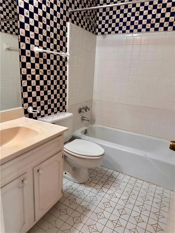 Bathroom with wallpapered walls, bathing tub / shower combination, vanity, and light tile patterned floors