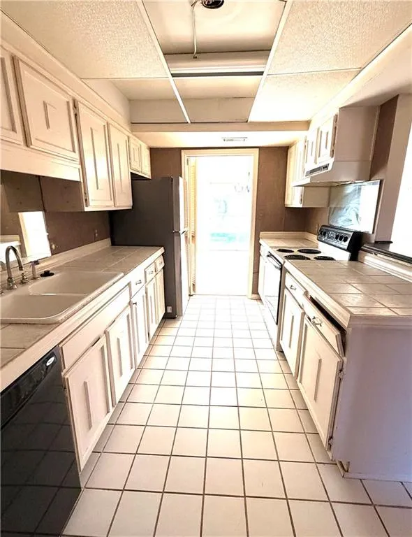 Kitchen featuring tile countertops, white range with electric stovetop, dishwasher, freestanding refrigerator, and light tile patterned flooring