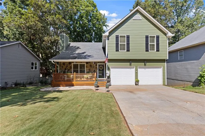 Split-level residence featuring a stone and siding exterior, a two-car garage, and a covered front deck