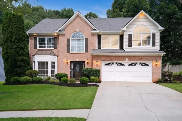 Brick and siding exterior with arched windows, a two-car garage, and a bay window