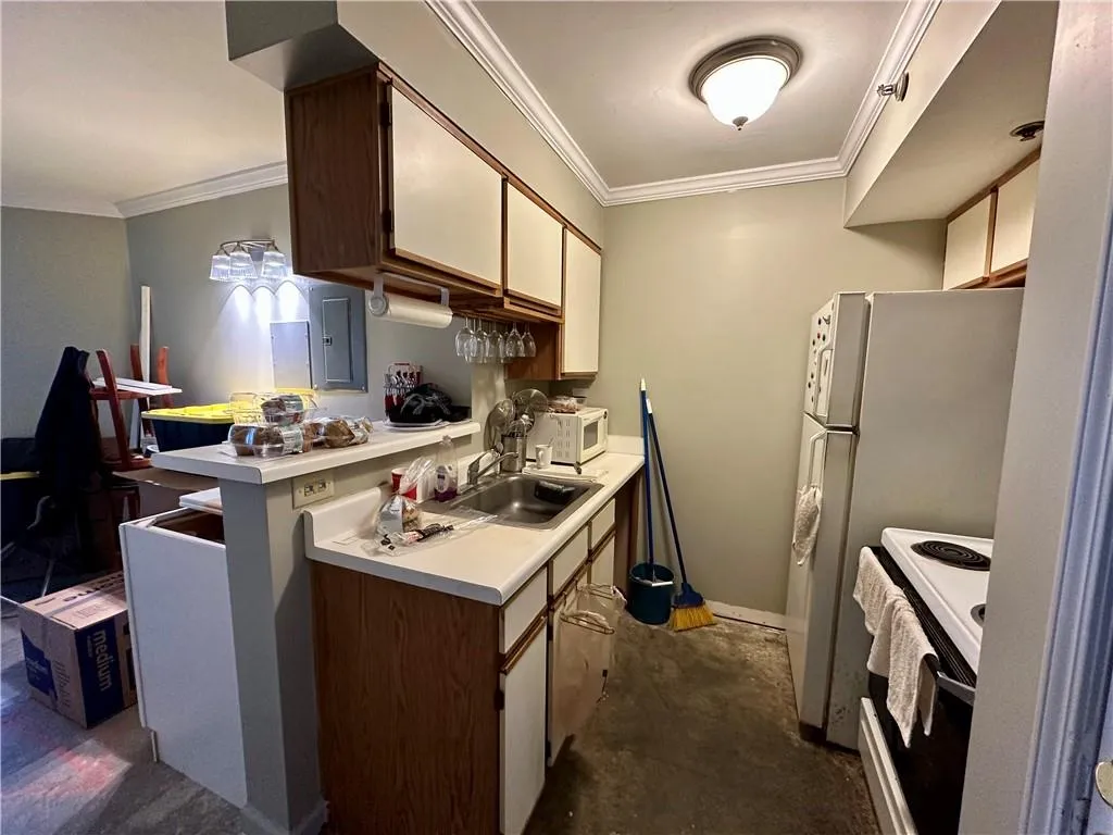 Kitchen with light countertops, crown molding, white appliances, concrete flooring, and a peninsula