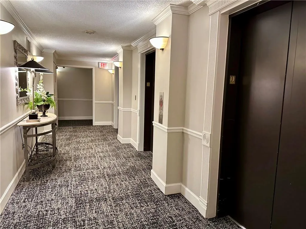 Hallway with a textured ceiling, dark colored carpet, elevator, and crown molding