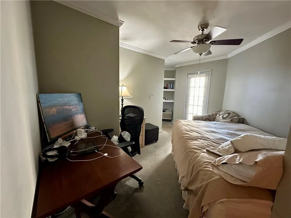 Carpeted bedroom featuring crown molding, ceiling fan, and an office area