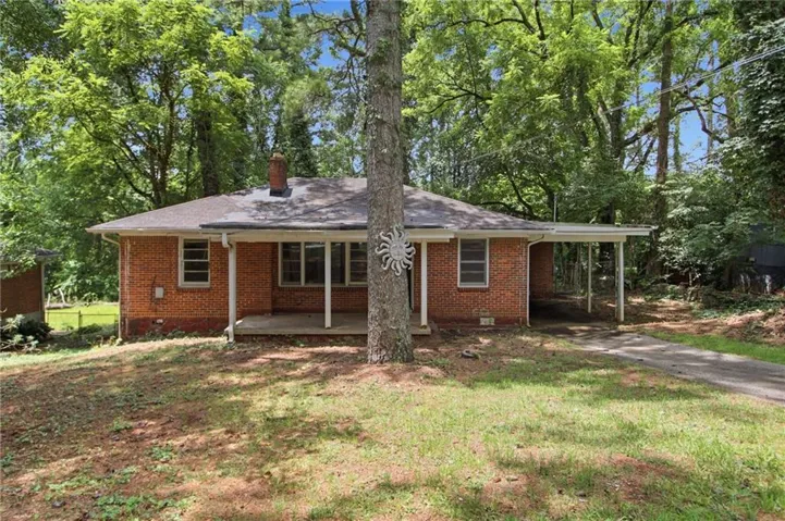 Brick exterior featuring a covered front porch, carport, and mature trees