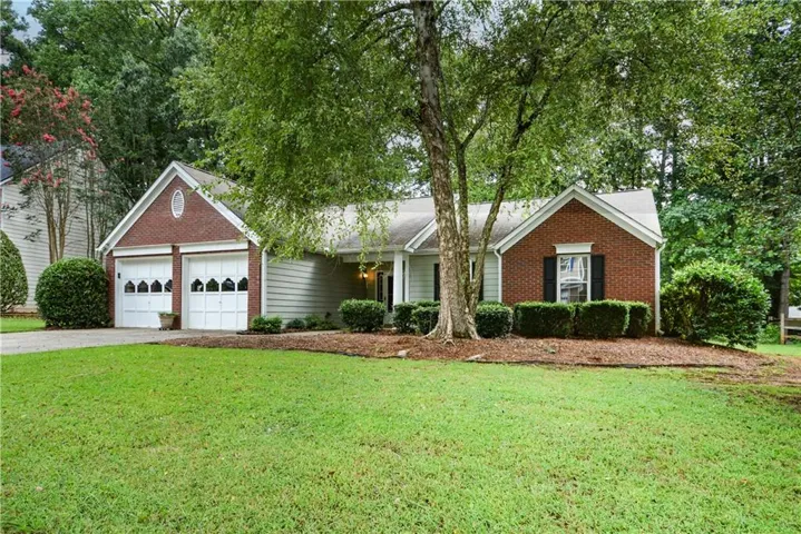 Brick and siding exterior, two-car garage with decorative doors, mature landscaping, established trees, and a well-maintained lawn
