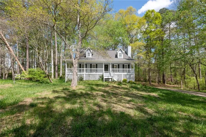 View of front facade with a front yard, covered porch, a chimney, and view of scattered trees