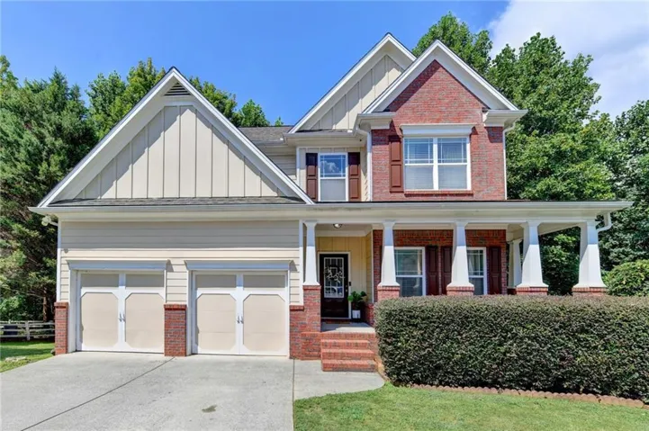 Two-story home featuring a brick and siding exterior, two-car garage, and a covered front porch with white columns