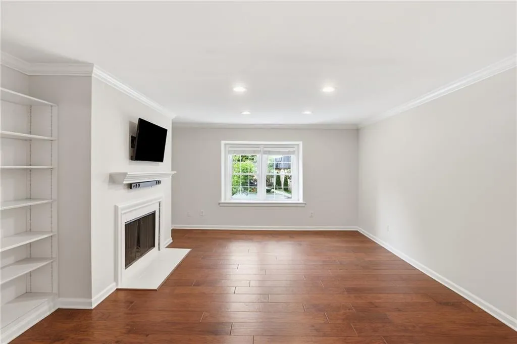 Spacious room featuring wood-finish flooring, a white mantel fireplace with a hearth, and built-in shelving