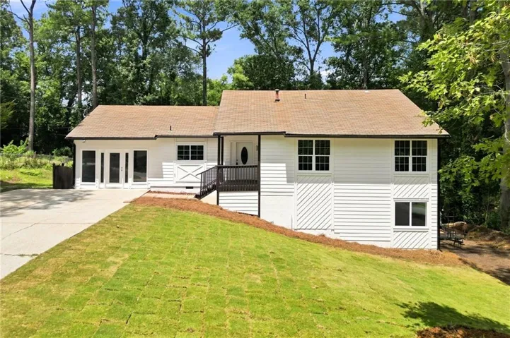 White siding exterior with a brown shingle roof, dark trim, and a prominent front entrance featuring a dark-stained deck with railing
