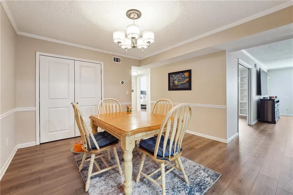 Dining area with wood-type flooring, a chandelier, crown molding, and a textured ceiling