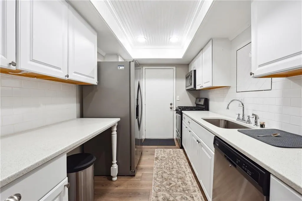 Kitchen with backsplash, stainless steel appliances, white cabinetry, and light wood-type flooring