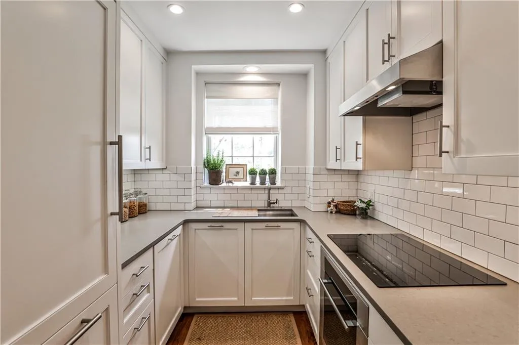 Kitchen featuring under cabinet range hood, black electric stovetop, oven, white cabinetry, and recessed lighting