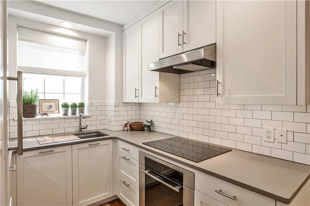 Kitchen featuring under cabinet range hood, oven, white cabinets, black electric cooktop, and decorative backsplash