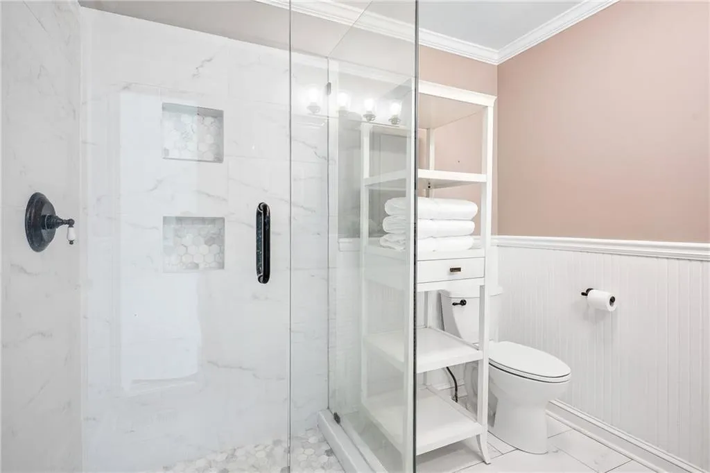 Full bath featuring a marble finish shower, crown molding, and a wainscoted wall