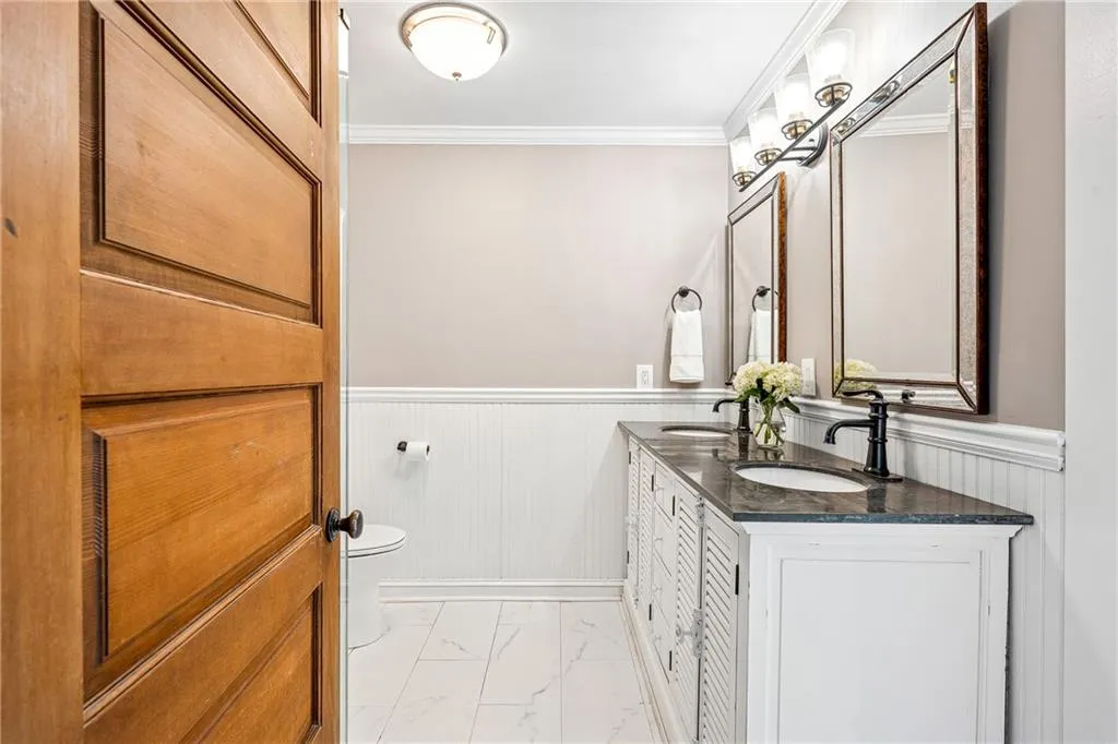 Full bath with double vanity, ornamental molding, wainscoting, and marble finish flooring