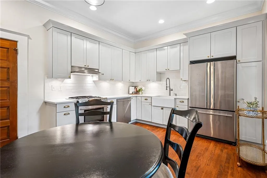 Kitchen featuring stainless steel appliances, dark wood-type flooring, crown molding, backsplash, and under cabinet range hood