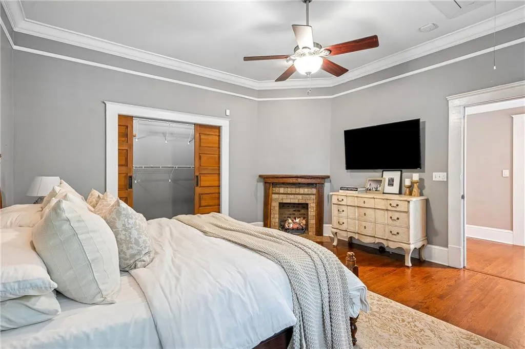 Bedroom featuring attic access, wood finished floors, ornamental molding, a spacious closet, and ceiling fan
