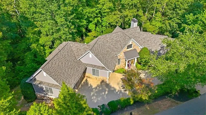 Expansive property featuring a multi-gabled roofline, stone and siding exterior, a prominent chimney, a covered entryway, and mature tree landscaping