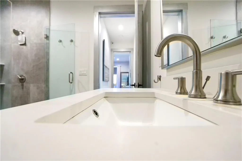 Vanity with an integrated rectangular sink, brushed nickel faucet, and a glass-enclosed shower with tiled walls