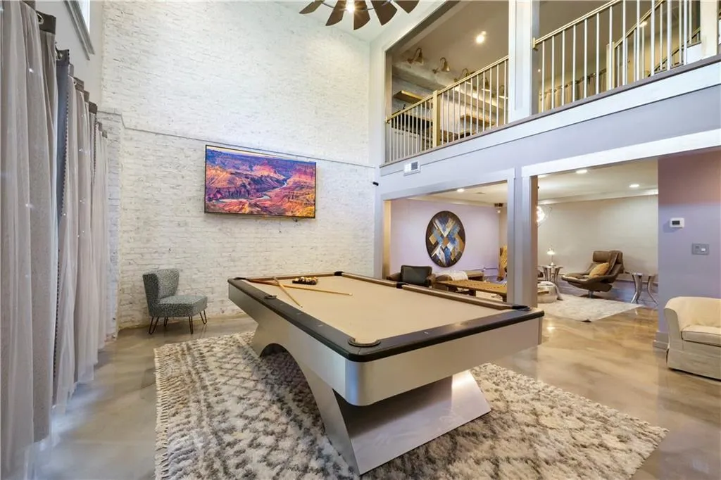 Two-story interior with an open-concept layout, exposed brick wall, polished concrete flooring, and a second-level balcony with metal railings