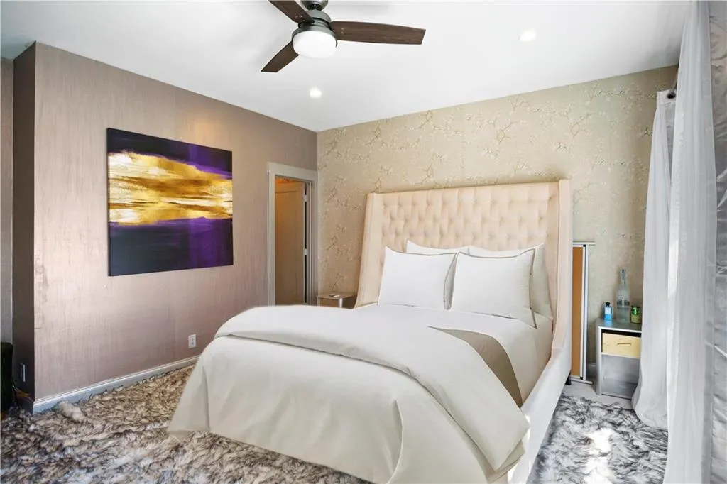 Tufted bed frame, recessed lighting, ceiling fan, textured wall finish, and wood-finish door frame