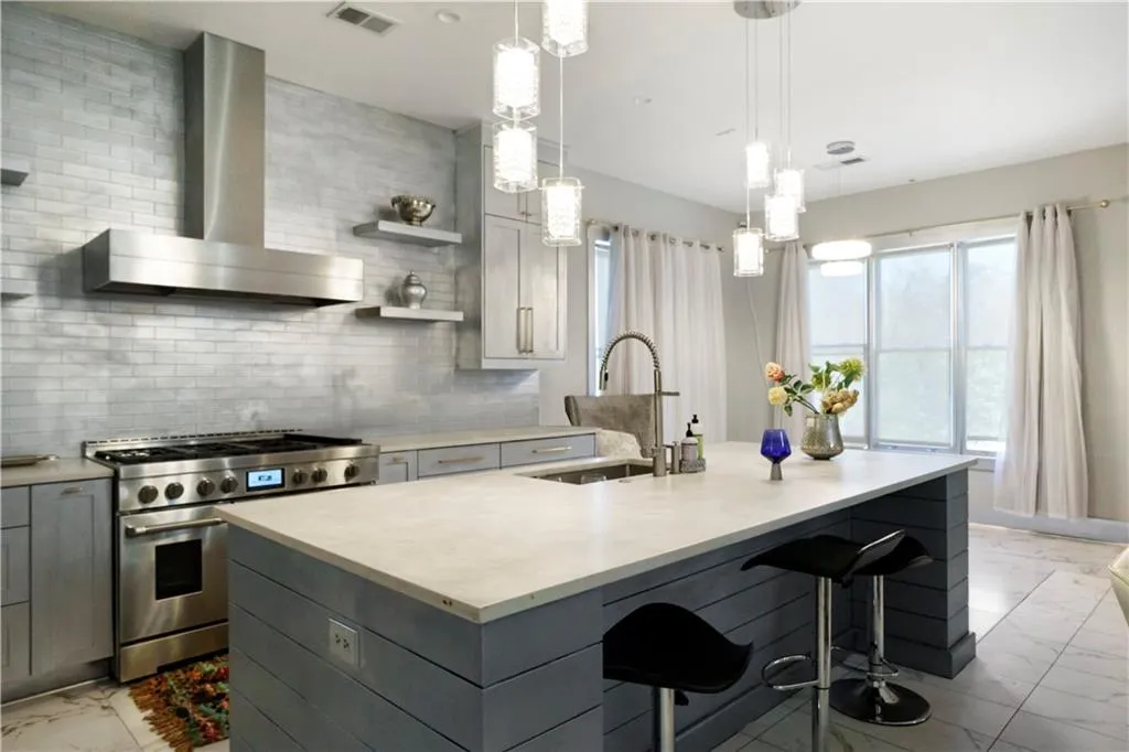 Gourmet kitchen with stainless steel range and hood, tile backsplash, built-in cabinetry, and a large island featuring a single basin sink and pendant lighting
