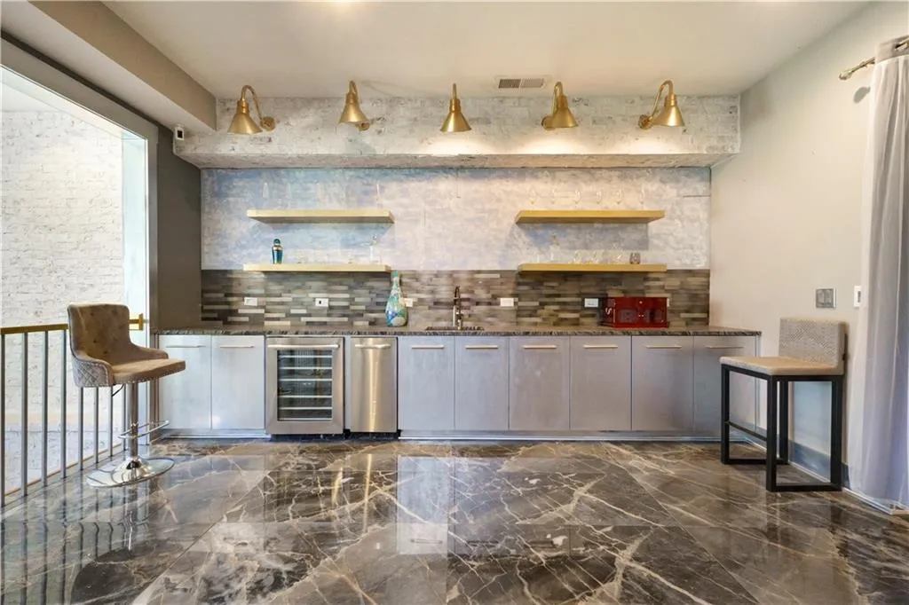 Wet bar with under-counter beverage cooler, stainless steel sink, wood-finish open shelving, and a multi-tone tile backsplash