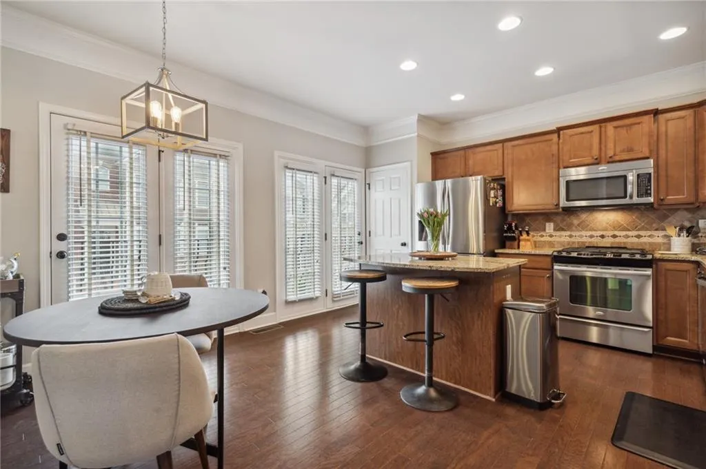 Kitchen with dark wood-type flooring, pendant lighting, stainless steel appliances, light stone countertops, and backsplash