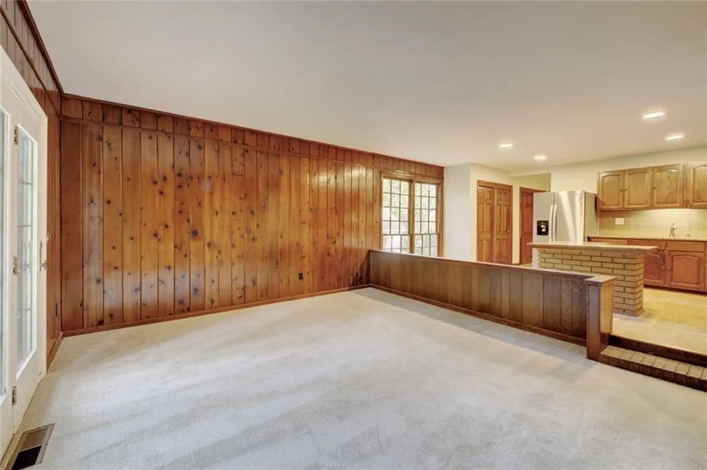 Unfurnished living room featuring carpet floors, wooden walls, and a brick fireplace