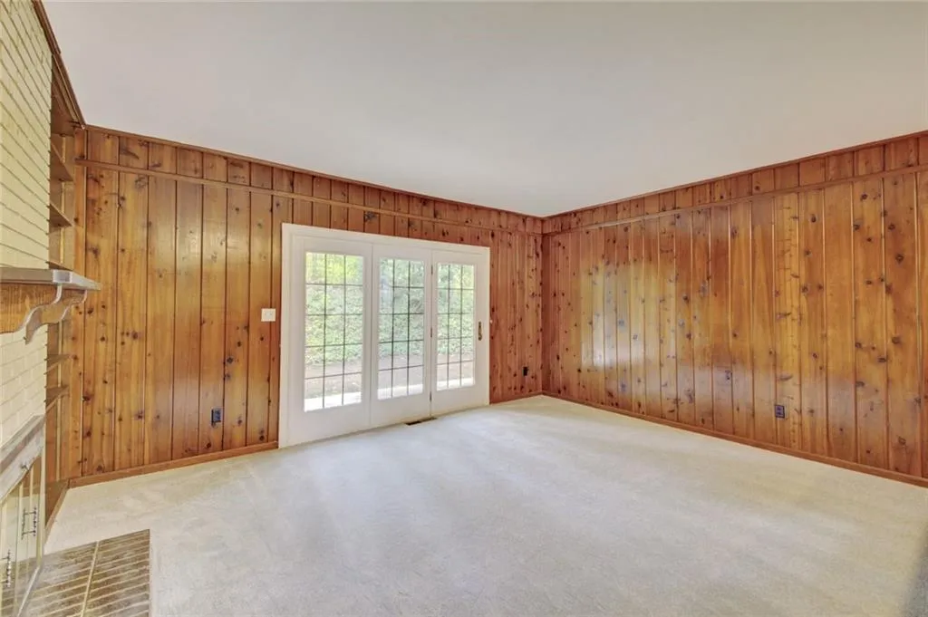 Unfurnished living room featuring carpet floors, wooden walls, and a brick fireplace