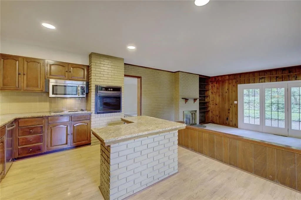 Kitchen with a fireplace, oven, brick wall, and light wood-type flooring