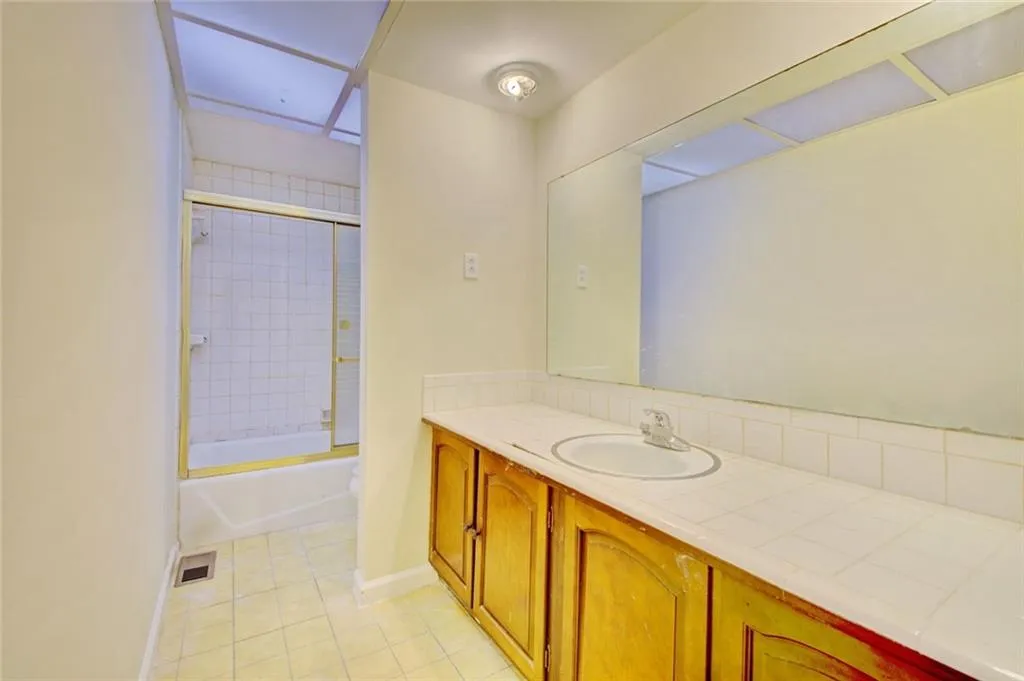 Bathroom with tile patterned flooring, shower / bath combination with glass door, and vanity