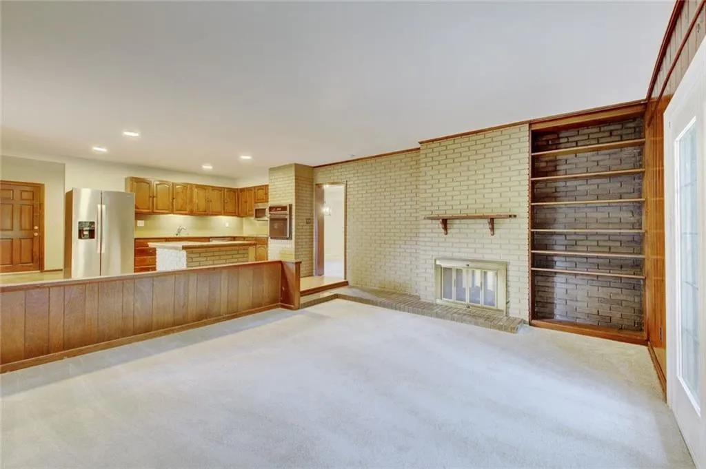 Unfurnished living room with light carpet, a brick fireplace, and brick wall