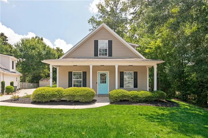 Traditional-style home featuring a covered front porch with white columns, tan siding, and black window shutters