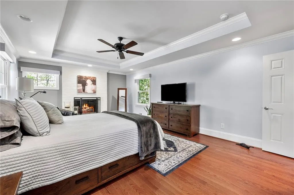 Bedroom with a tray ceiling, wood finished floors, multiple windows, and a brick fireplace