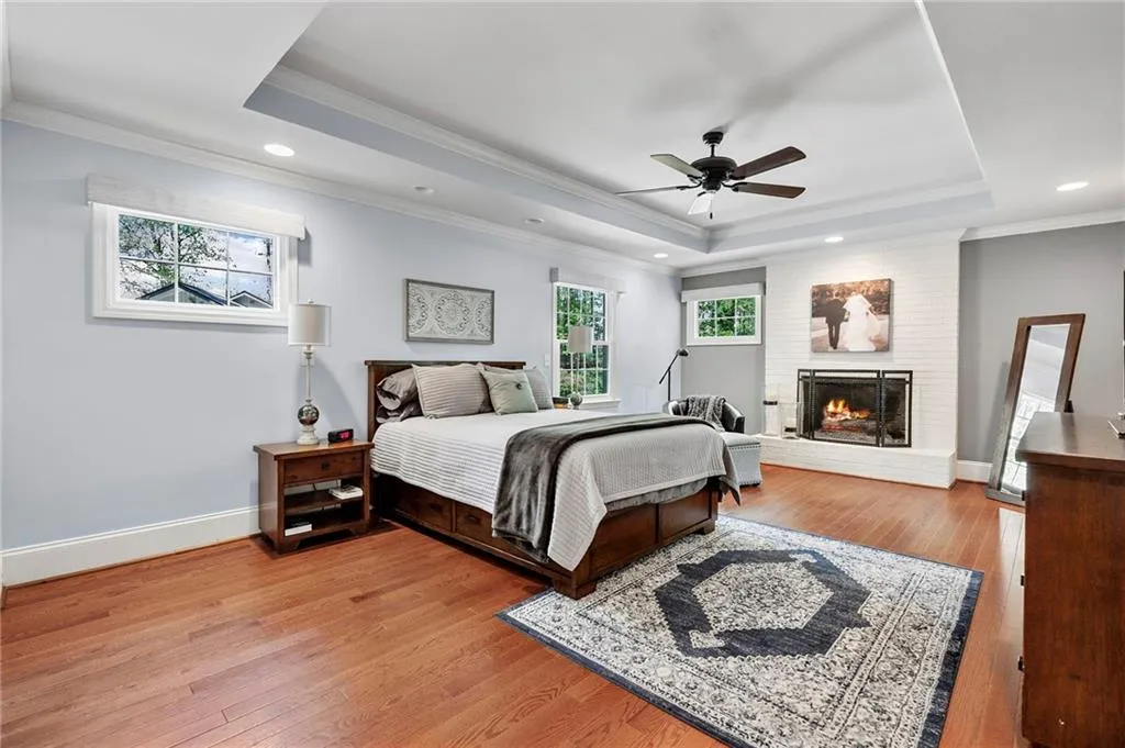 Bedroom with ornamental molding, recessed lighting, a fireplace, a tray ceiling, and wood finished floors
