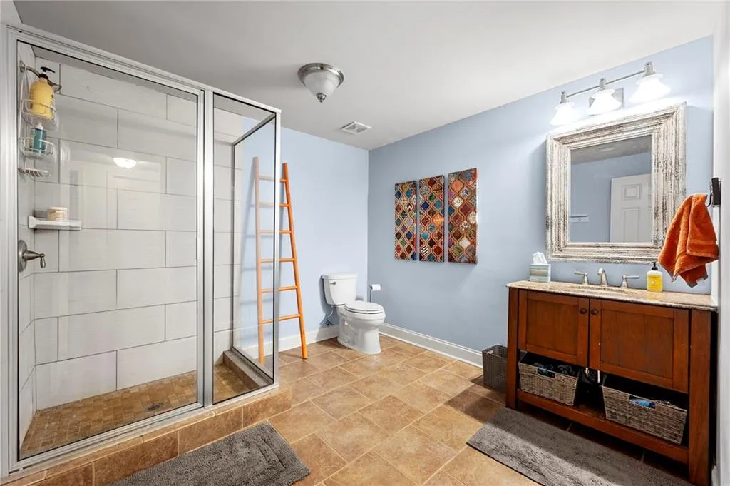 Bathroom featuring toilet, a stall shower, vanity, and baseboards