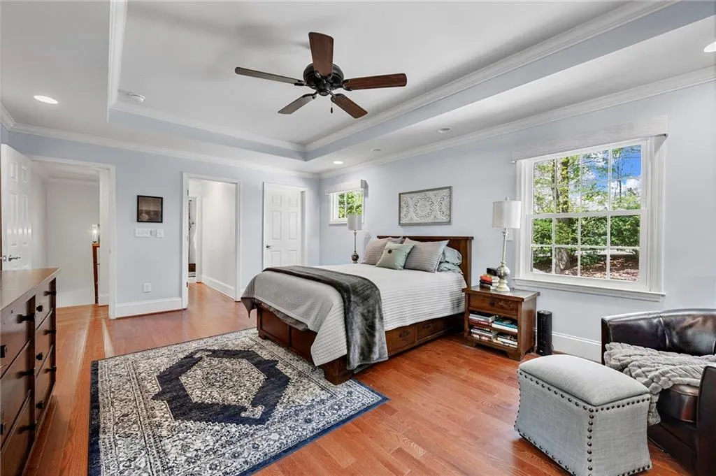 Bedroom with baseboards, a raised ceiling, crown molding, ceiling fan, and light wood finished floors