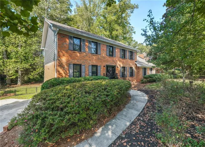 Brick exterior with gray shutters, mature landscaping, and a paved walkway leading to the entrance