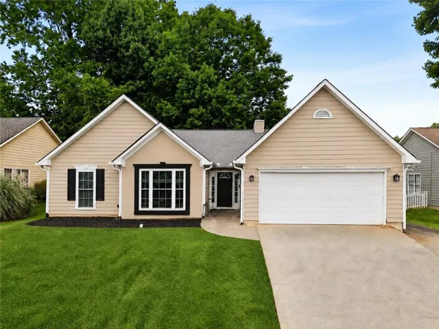 Beige siding exterior with black shutters, a two-car garage, and a concrete driveway