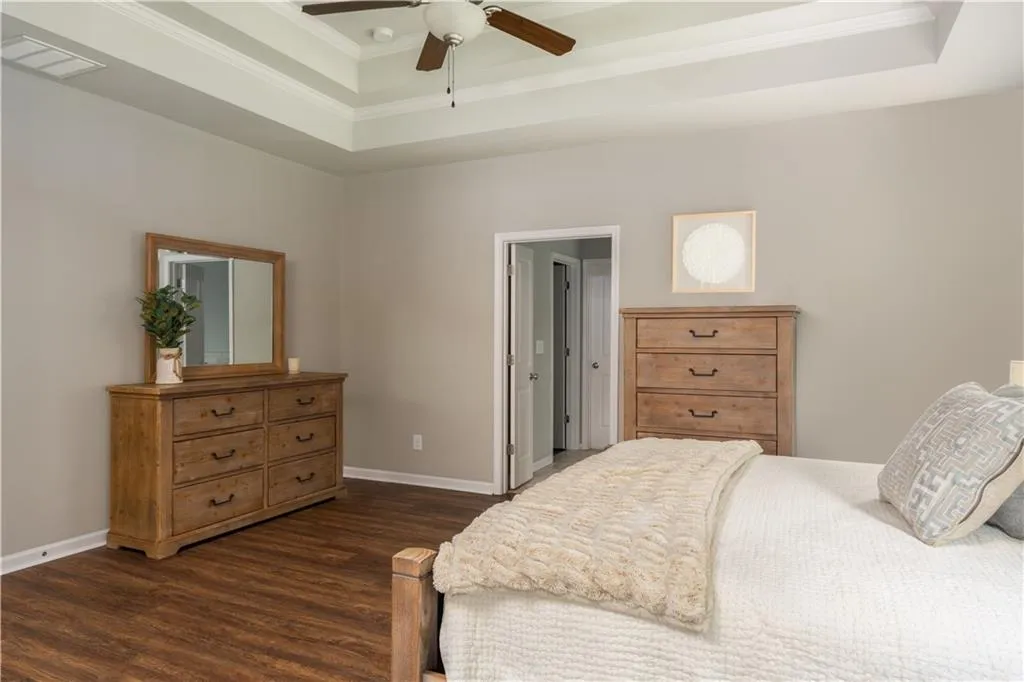 Bedroom featuring a raised ceiling, dark wood finished floors, crown molding, and ceiling fan