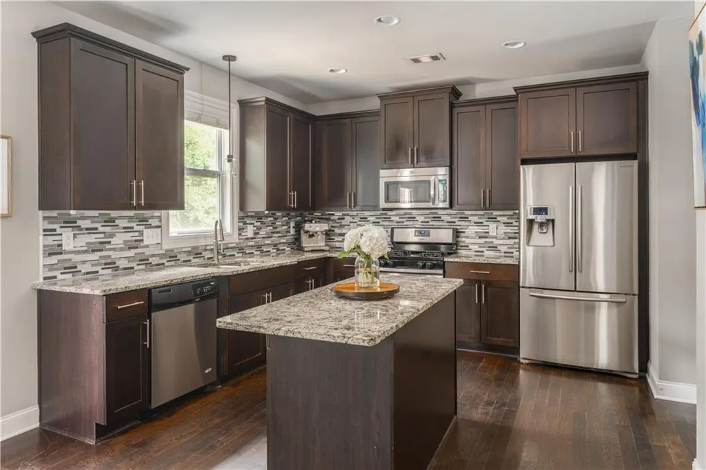 Kitchen featuring stainless steel appliances, dark brown cabinetry, light stone countertops, dark wood-style flooring, and decorative backsplash