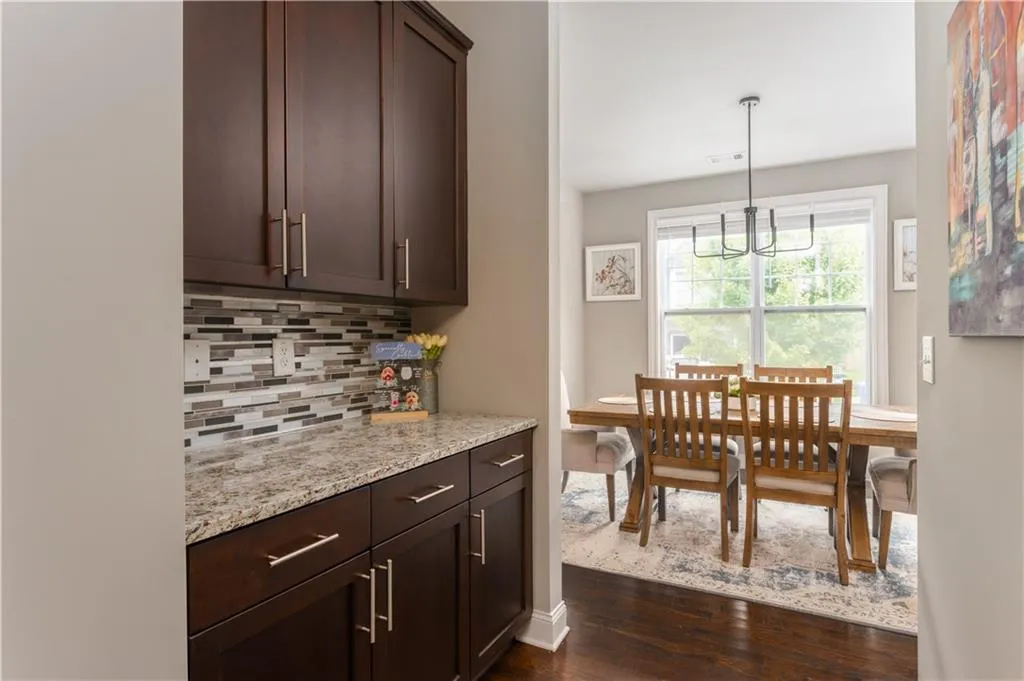 Kitchen with dark wood-style floors, dark brown cabinets, tasteful backsplash, light stone counters, and decorative light fixtures